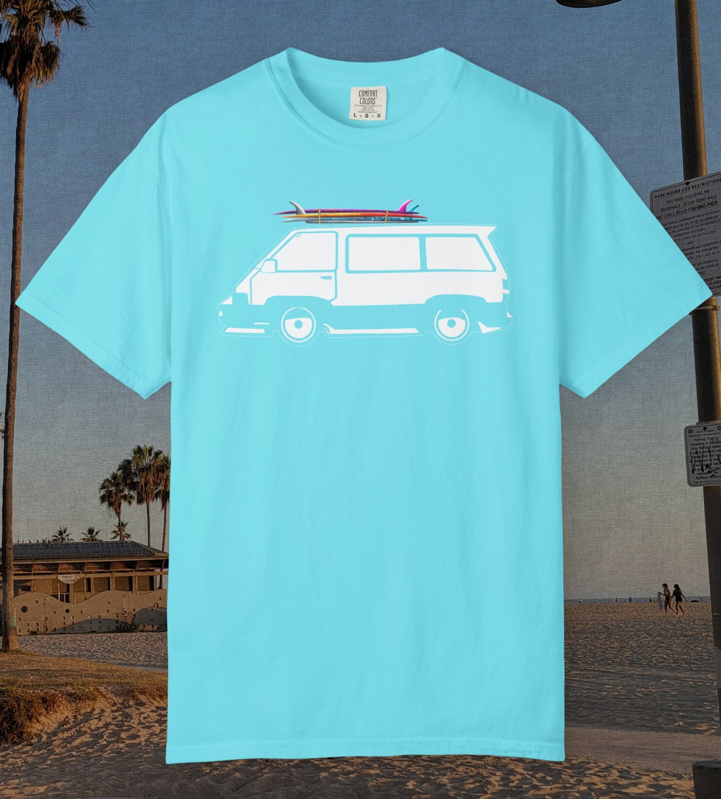 A lagoon blue short-sleeve t-shirt with a white graphic of a van carrying surfboards, displayed against a beach background.