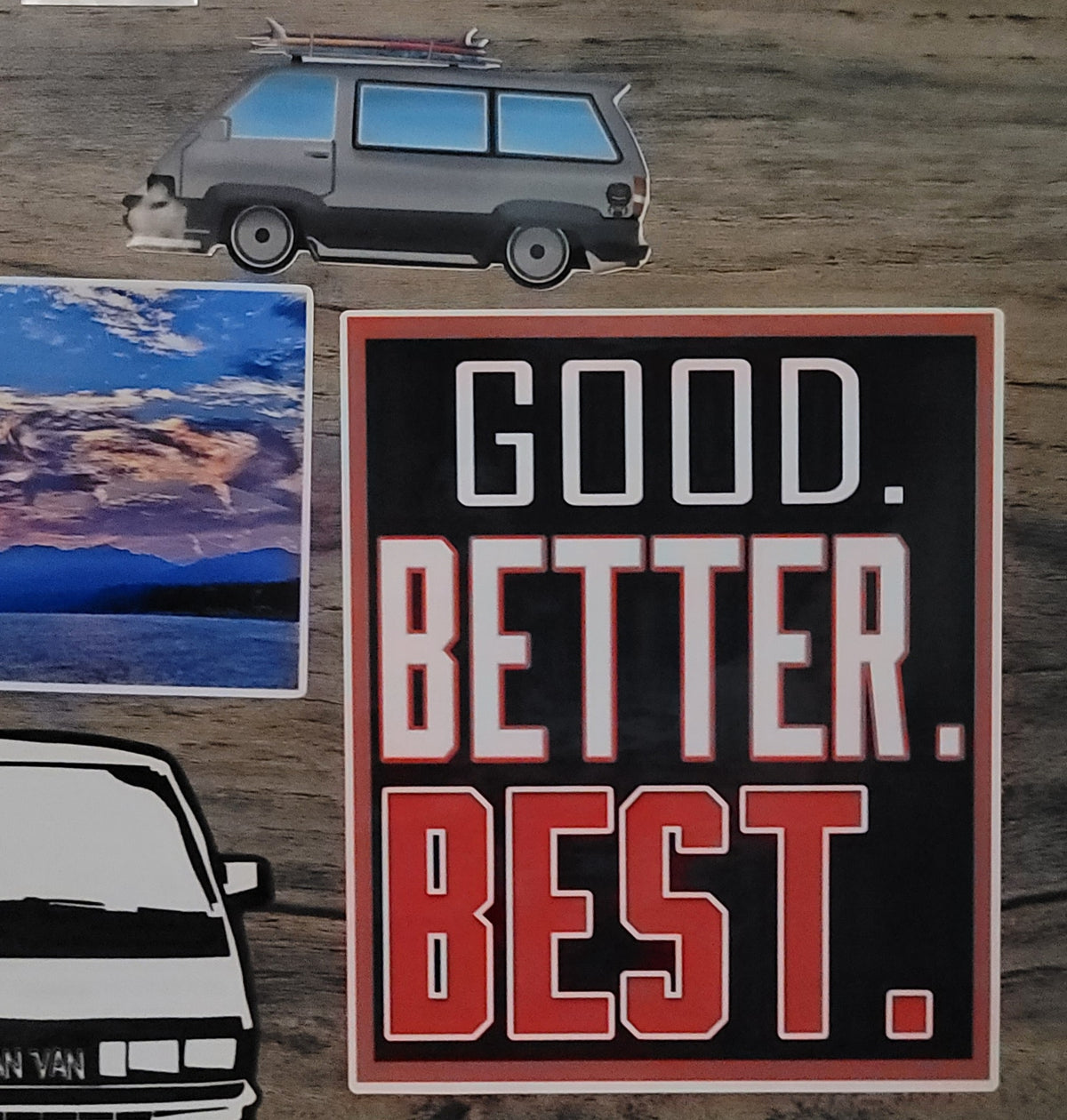 3.75" x 4" sticker with 'Good. Better. Best.' On background that also has van stickers, and a scenic sticker on a wooden background.