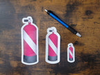 Three red and white dive flag scuba tank stickers on a wooden surface with a pen for size reference.