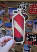 Hand holding a red and white dive flag scuba diving tank sticker against a background of various other stickers.