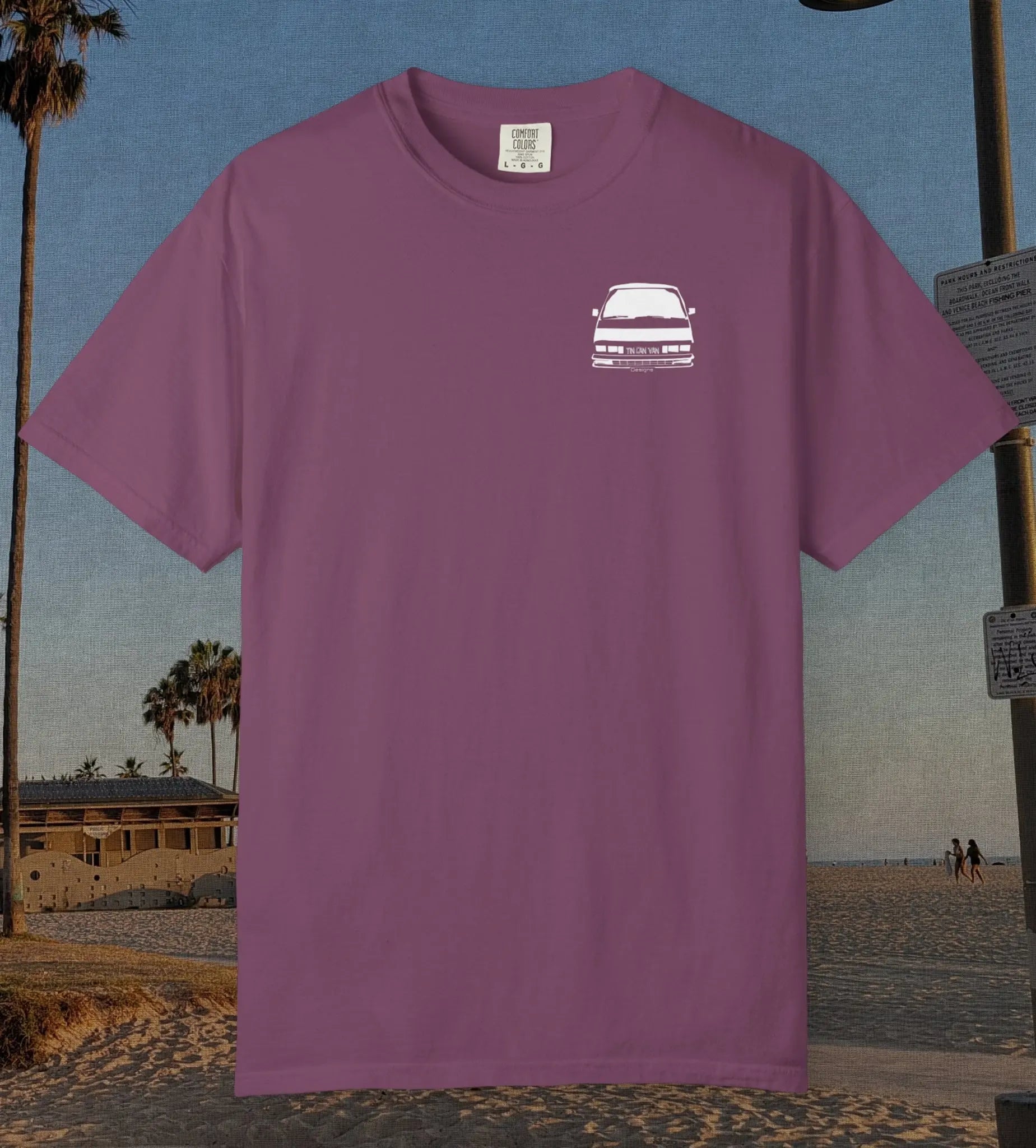 A berry short-sleeve t-shirt with a small white graphic of a car on the left chest, displayed against a beach background.