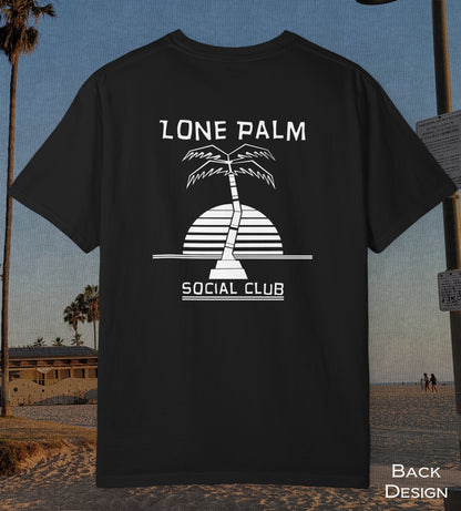 A black short-sleeve t-shirt with a white graphic print of a palm tree and the text 'LONE PALM SOCIAL CLUB' on the back, displayed against a beach background.