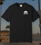 A black short-sleeve t-shirt with a small white graphic of a car and the text 'I'M NOT SLEEPING' on the left chest, displayed against a beach background.