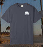 A navy t-shirt with a small white graphic of a classic car on the left chest, displayed against a beach background.