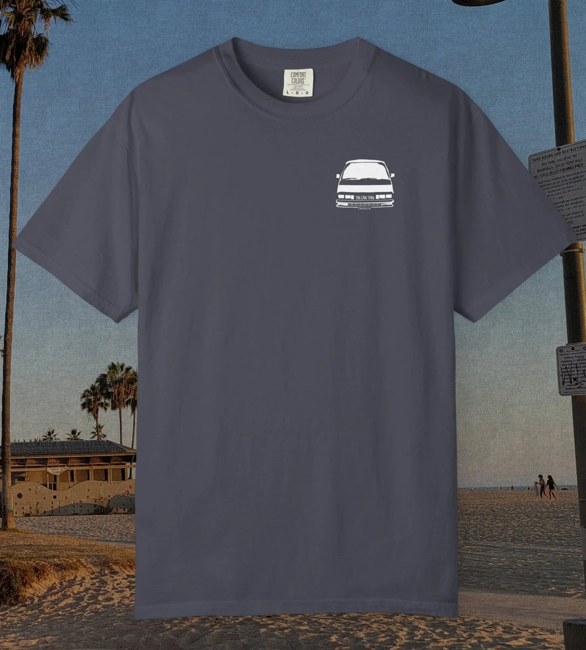 A navy t-shirt with a small white graphic of a classic car on the left chest, displayed against a beach background.