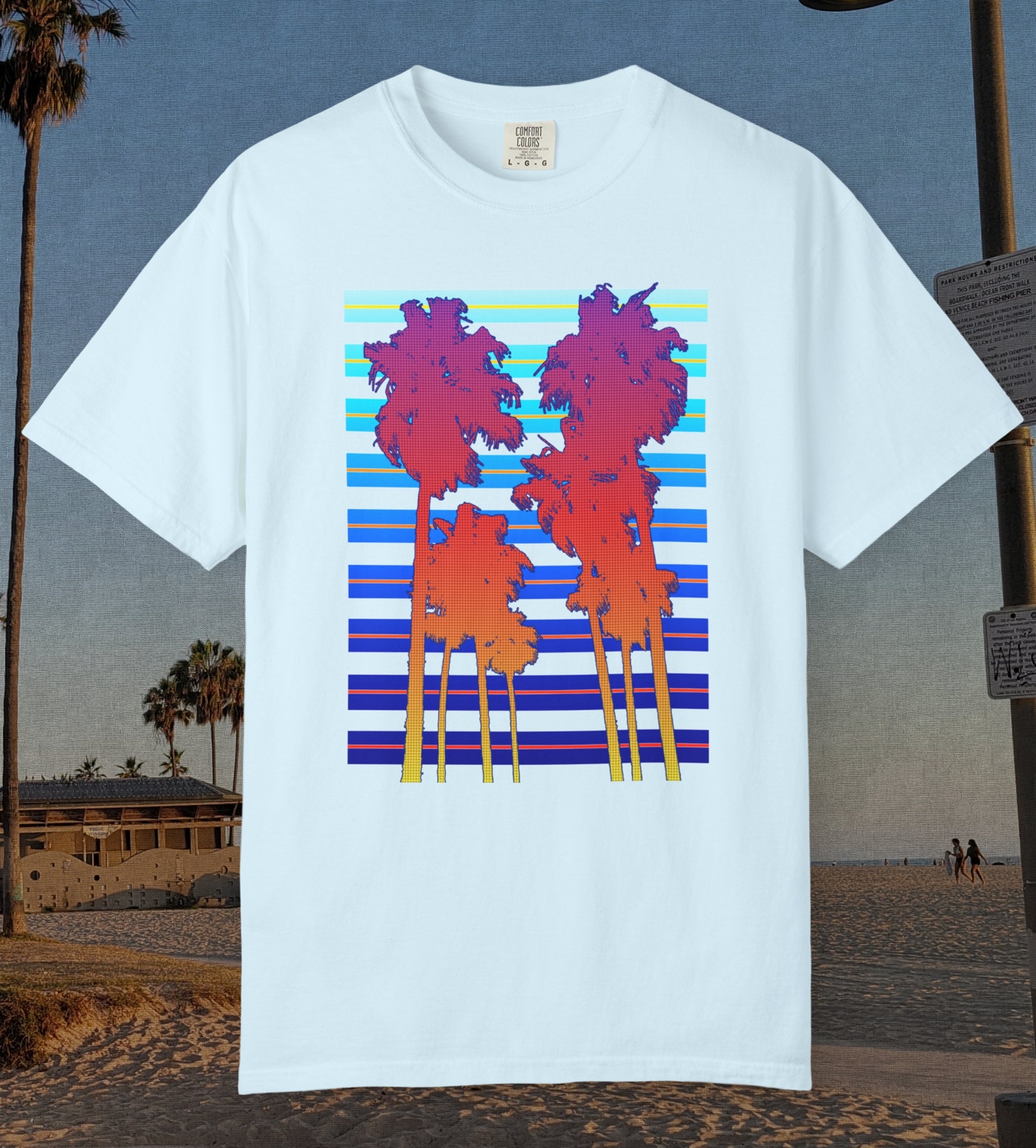 Comfort Colors cotton t-shirt Chambray/Light blue in color featuring a DTF graphic of palm tree silhouettes in warm colors with a cool color background pattern.