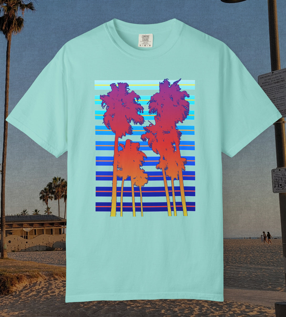 Comfort Colors cotton t-shirt Chalky Mint Green in color featuring a DTF graphic of palm tree silhouettes in warm colors with a cool color background pattern.