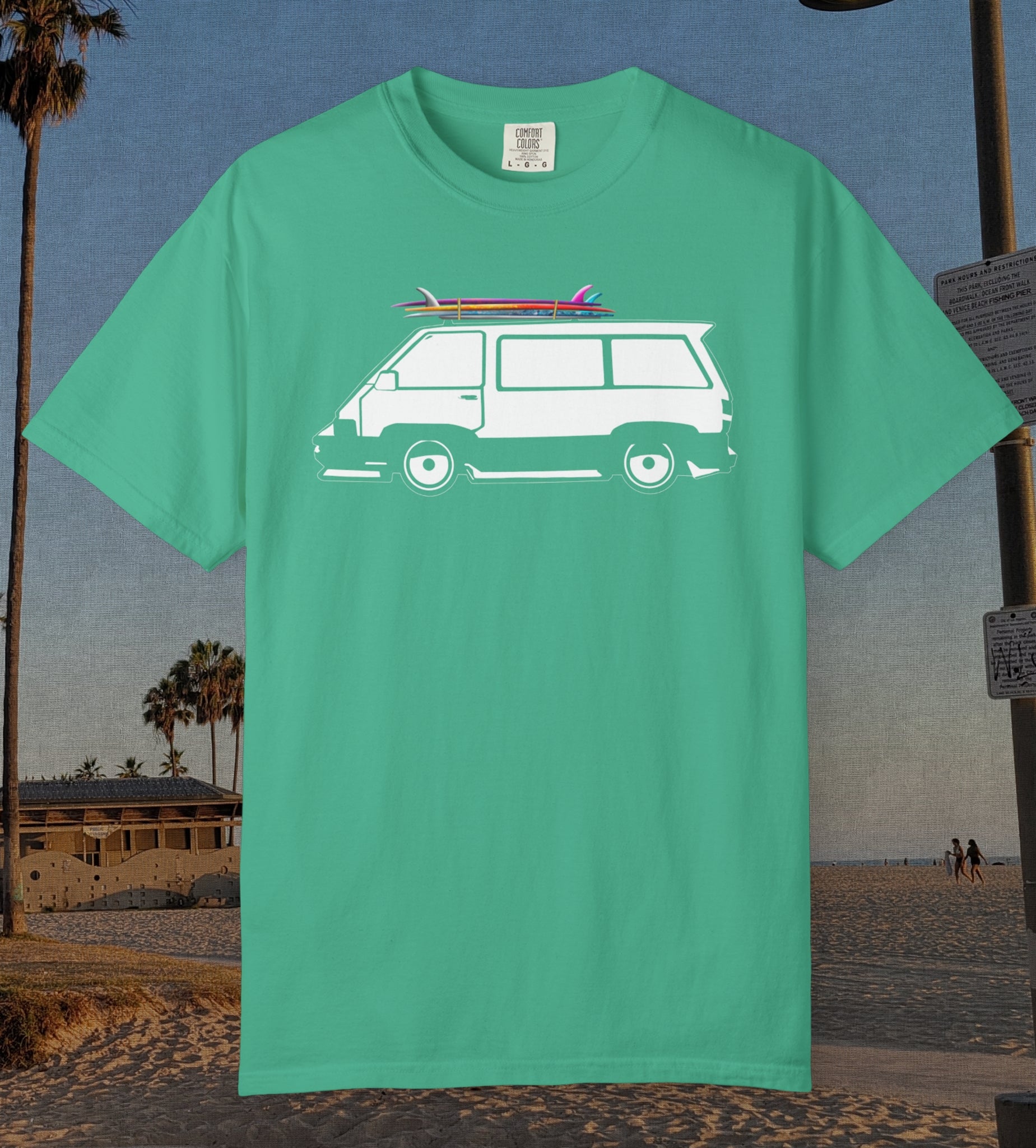 A island green short-sleeve t-shirt with a white graphic of a vintage van carrying surfboards on its roof, displayed against a beach background.