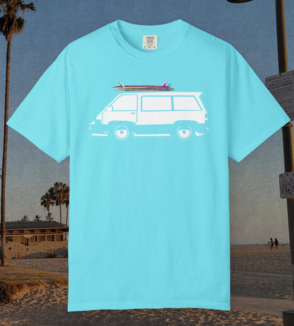 A lagoon blue short-sleeve t-shirt with a white graphic of a van carrying surfboards, displayed against a beach background.