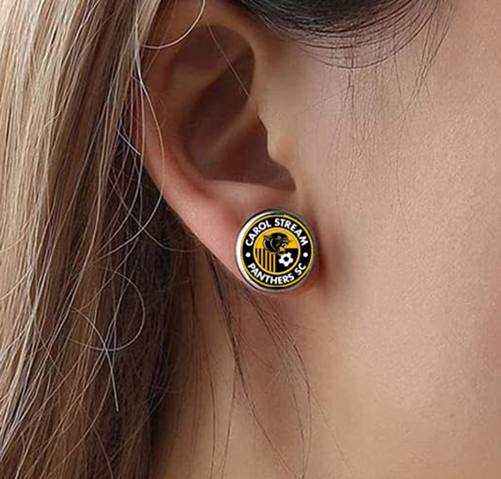 A close-up of a person's ear wearing a round stainless steel earring featuring the Carol Stream Panthers Soccer Club Logo.