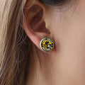 A close-up of a person's ear wearing a round stud earring with the Carol Stream Panthers SoccerClub logo and team name.