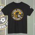A black short-sleeve t-shirt featuring a circular 'Carol Stream Panthers SC' graphic on the chest, with a yellow and white soccer theme and a panther illustration. The shirt is displayed flat against a gray background with a blurred version of the graphic on the left.