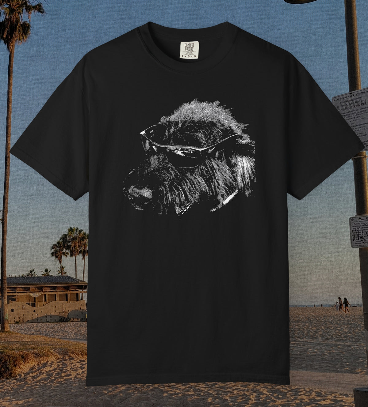 A black short-sleeve t-shirt featuring a white graphic print of a dog wearing sunglasses, displayed against a beach background.