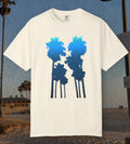 An ivory comfort colors short-sleeve t-shirt with a graphic of two palm tree silhouettes in light blue to navy blue gradient, displayed against a beach background.